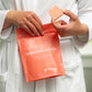 Person holding a package of Grapefruit Garden shower steamer by The Herbal Zen in their right hand and a single shower steamer in their left hand.